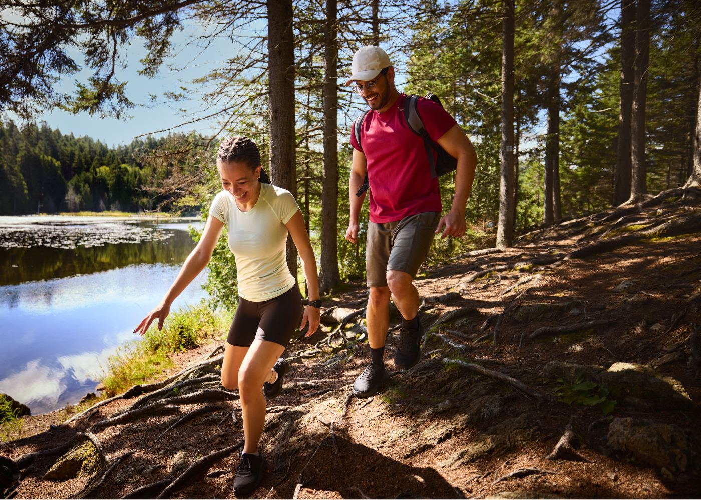 Two hikers on a forest trail beside a lake