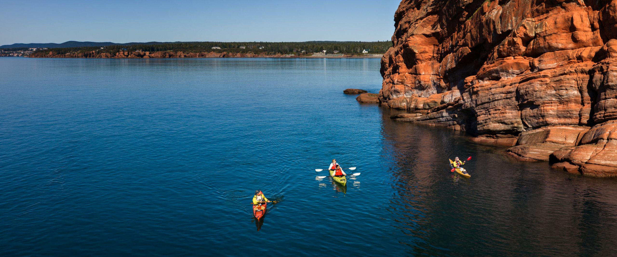 Sea kayakers paddling past red sandstone cliffs on the Bay of Fundy