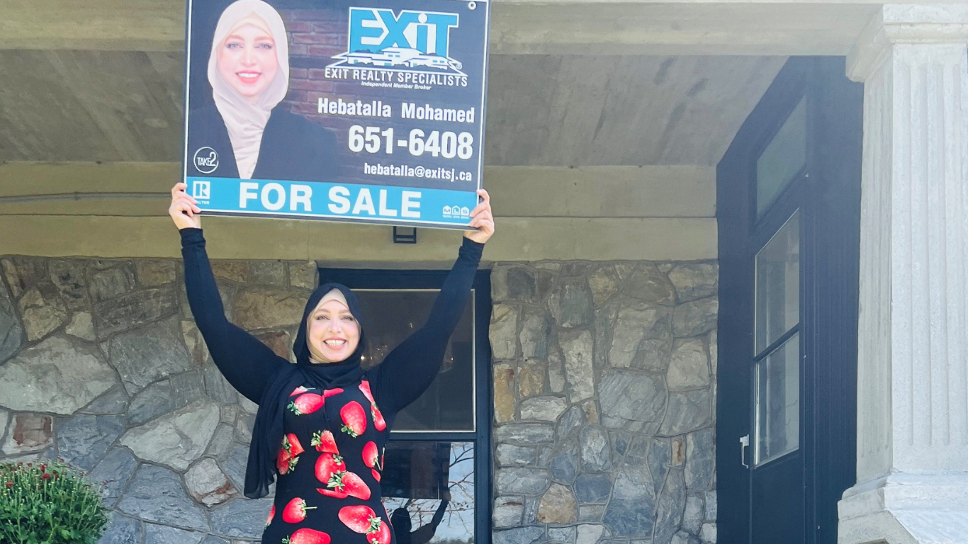 woman standing holding a house for house sold sign