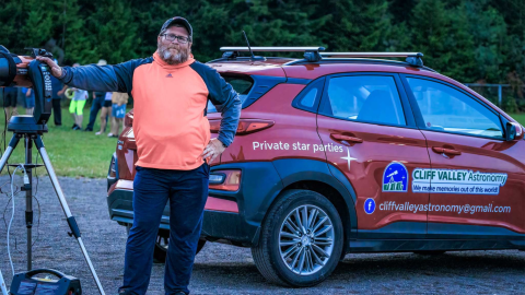 man standing with telescope in front of car