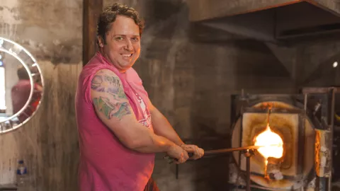 man smiling at camera blowing glass 
